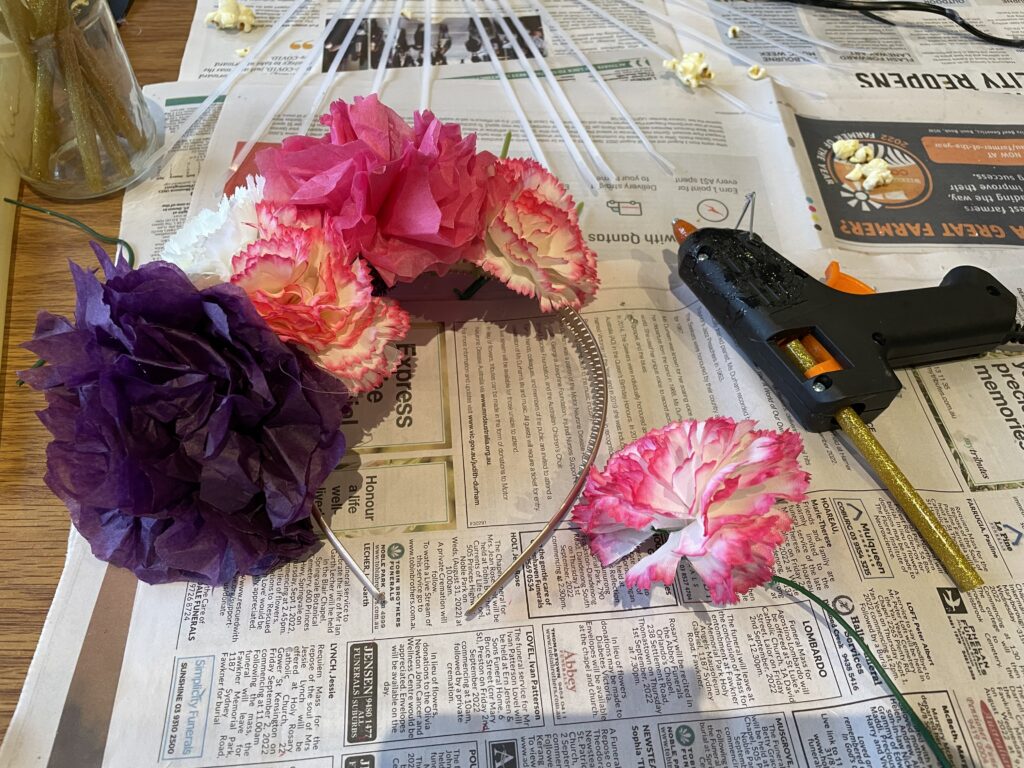 diadema con flores de papel y seda dispuestas sobre ella con una pistola de pegamento al lado