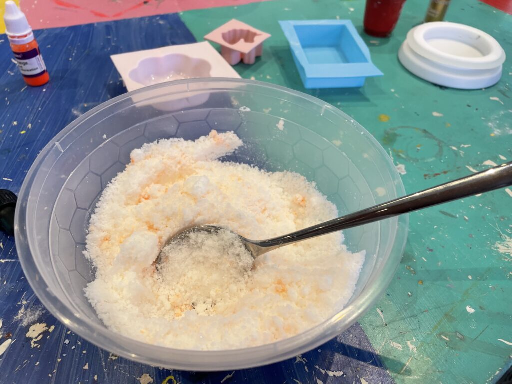 tazón con ingredientes de bomba de baño de naranja con cuchara mezcladora.